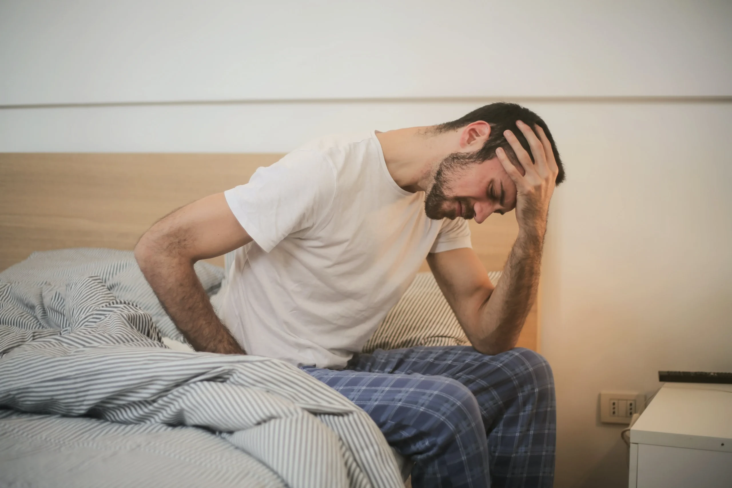 Man sitting on edge of bed holding his head 